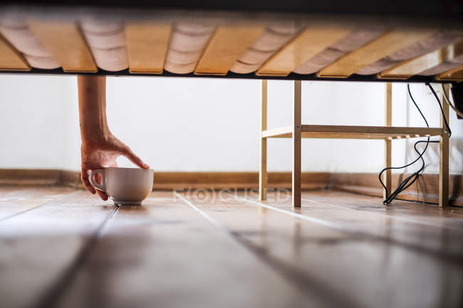 Mão das mulheres tomando copo debaixo da cama — Fotografia de Stock