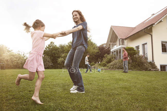 Mãe e filha dançando no jardim com a família no fundo — Fotografia de Stock