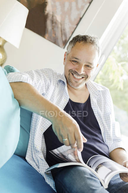 Человек сидит на диване с журналом — стоковое фото
