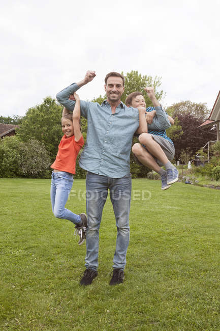 Retrato de pai feliz carregando seus dois filhos no jardim — Fotografia de Stock
