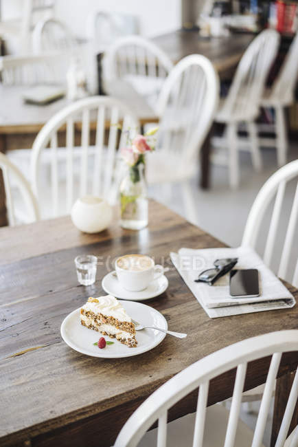 Celular, óculos de sol, bolo e xícara de café na mesa em um café — Fotografia de Stock