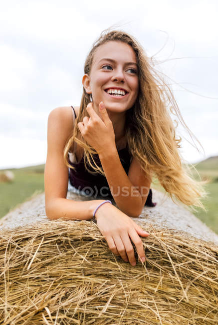 Portrait of smiling blond teenage girl lying on straw bale — Stock Photo
