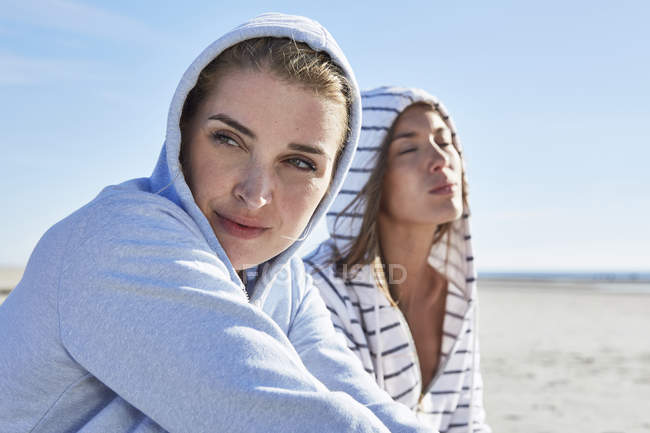 Due amiche che indossano felpe sedute sulla spiaggia — Foto stock