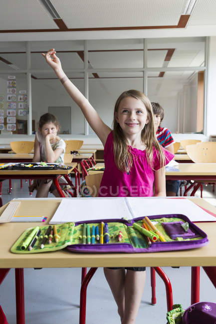 Portrait of smiling schoolgirl with raising hand sitting at class — Stock Photo