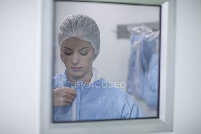 Woman behind glass pane putting on sterile protective clothing — Stock Photo