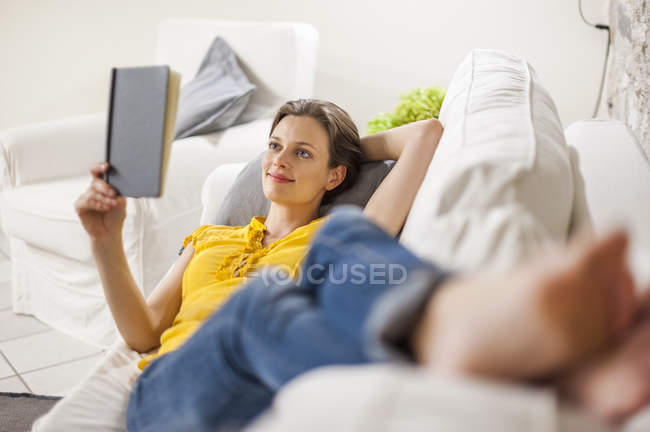 Woman lying on couch and reading a book — Stock Photo