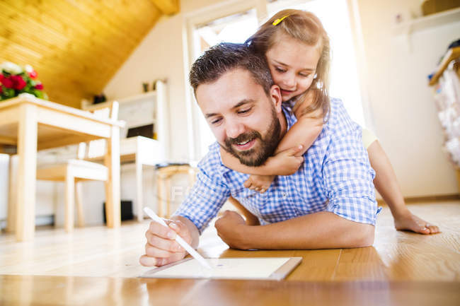 Father and daughter lying on floor, drawing on digital tablet — Stock Photo