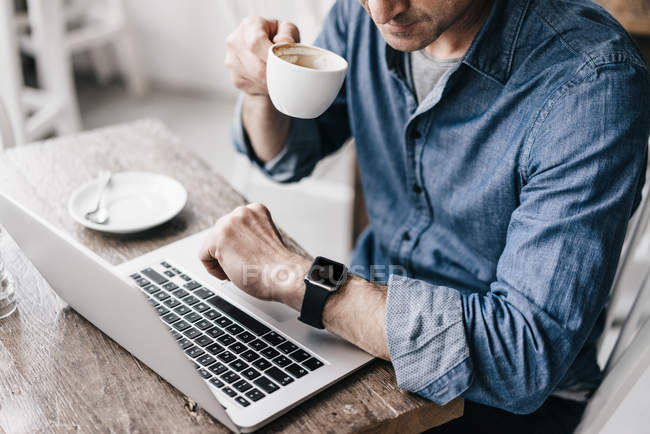 Человек пьет кофе во время работы на ноутбуке — стоковое фото