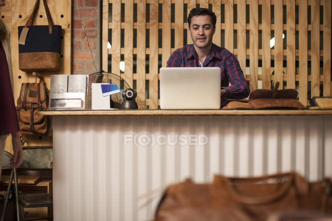Man using laptop on shop counter — Stock Photo