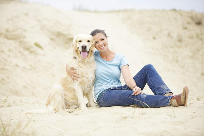 Sonriente joven con perro en la arena - foto de stock
