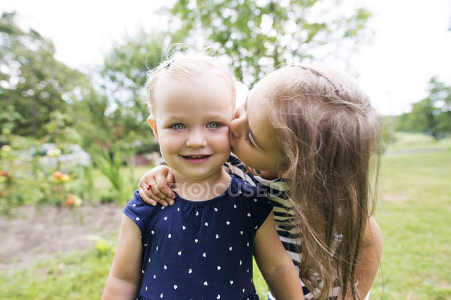 Mädchen küsst kleine Schwester im Garten — Stockfoto