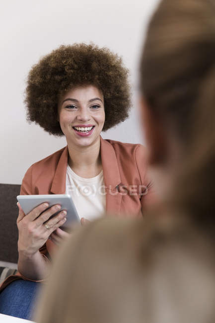 Sorrindo jovem mulher com tablet em um café olhando para a mulher — Fotografia de Stock
