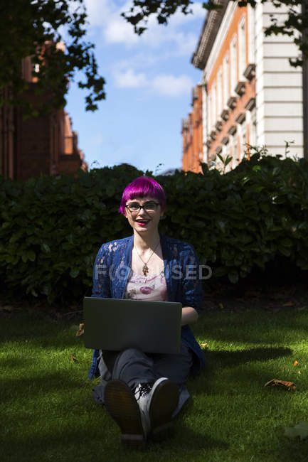 Молода жінка з пофарбованих волосся сидить на луг, використовуючи ноутбук — стокове фото
