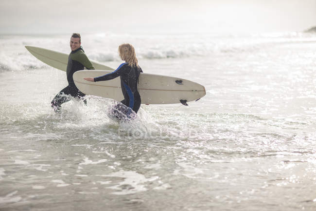 Coppia con tavole da surf che attraversano le onde — Foto stock