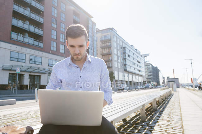 Uomo d'affari seduto sul banco utilizzando il computer portatile — Foto stock