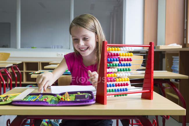 Улыбающаяся школьница сидит за столом в классе — стоковое фото