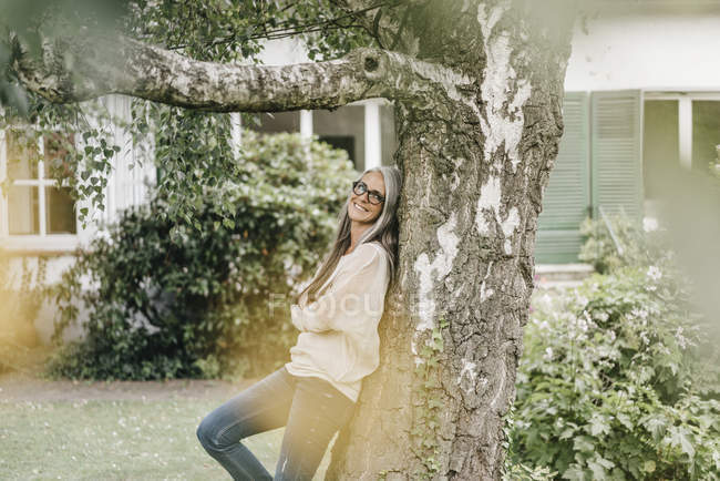 Donna sorridente appoggiata all'albero — Foto stock