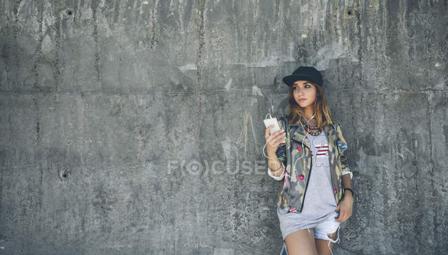 Giovane donna appoggiata al muro di cemento ascoltare musica con gli auricolari — Foto stock
