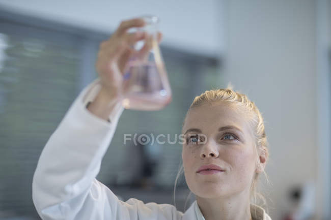 Jeune femme en laboratoire examinant le liquide dans une fiole Erlenmeyer — Photo de stock