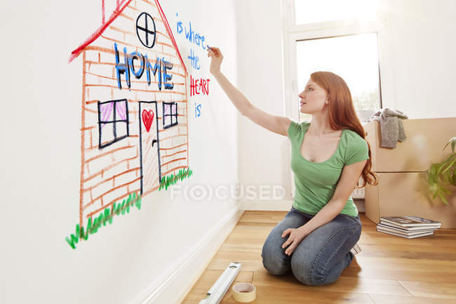 Jovem mulher desenhando uma casa em uma parede no novo apartamento — Fotografia de Stock