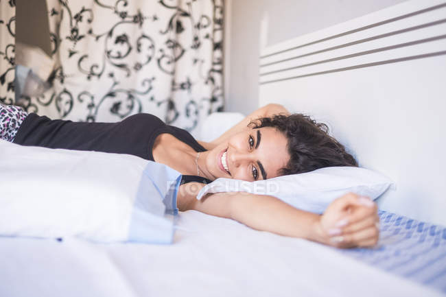 Portrait of smiling teenage girl lying on bed stretching her arms — Stock Photo