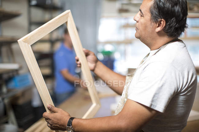 Hombre mirando el marco de madera para la preparación de lona en taller - foto de stock