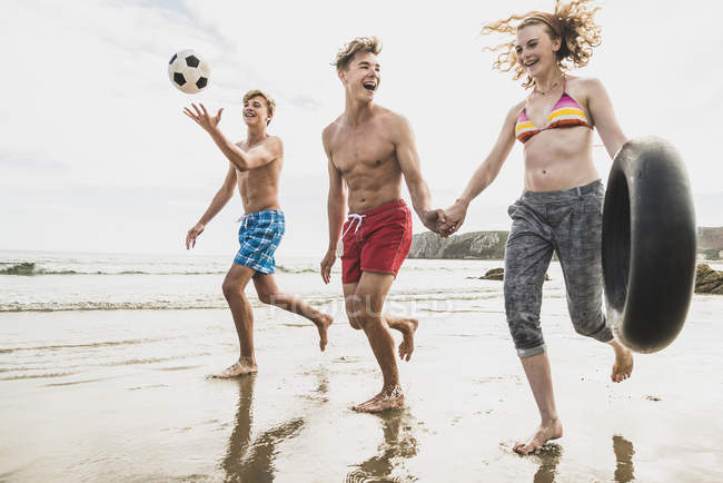 Amigos correndo com uma bola e pneu na praia — Fotografia de Stock