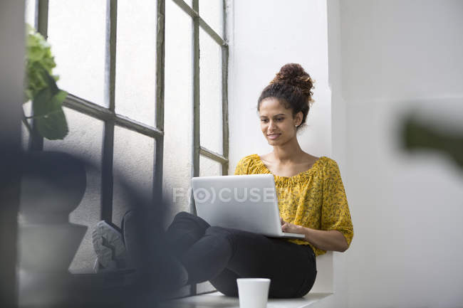Mujer sentada en la ventana y el alféizar usando portátil - foto de stock