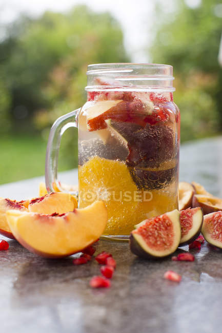 Jar of infused water with orange slices, fig, pomegranate seeds, nectarine and plums — Stock Photo