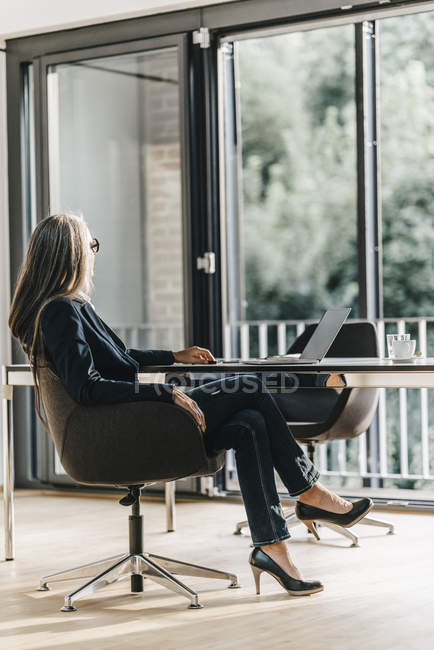 Businesswoman sitting with laptop at desk in office — Stock Photo