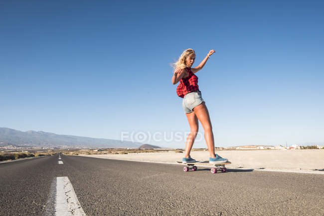 Jeune belle fille blonde chevauchant sur skateboard en plein air — Photo de stock