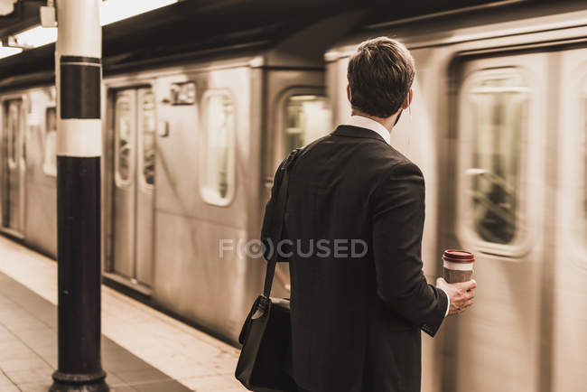 Young businessman waiting at metro station platform and holding disposable cup — Stock Photo