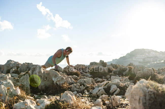 Спортсмен отжимается на скалистом побережье утром — стоковое фото