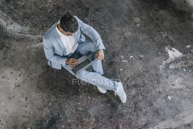 Businessman sitting on concrete floor and using laptop — Stock Photo