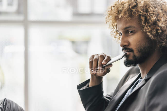 Joven empresario reflexivo sosteniendo teléfono inteligente - foto de stock