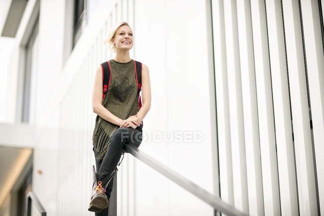 Portrait de femme blonde souriante assise sur une balustrade — Photo de stock