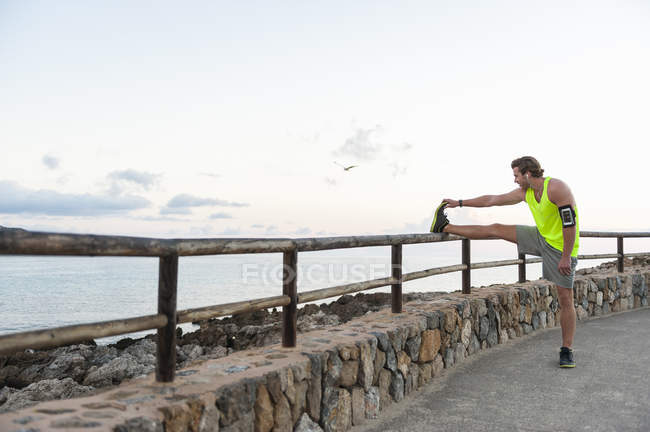 Jogger allungamento gamba sulla recinzione di legno in mare — Foto stock