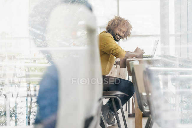 Young man sitting at table and working with laptop — Stock Photo