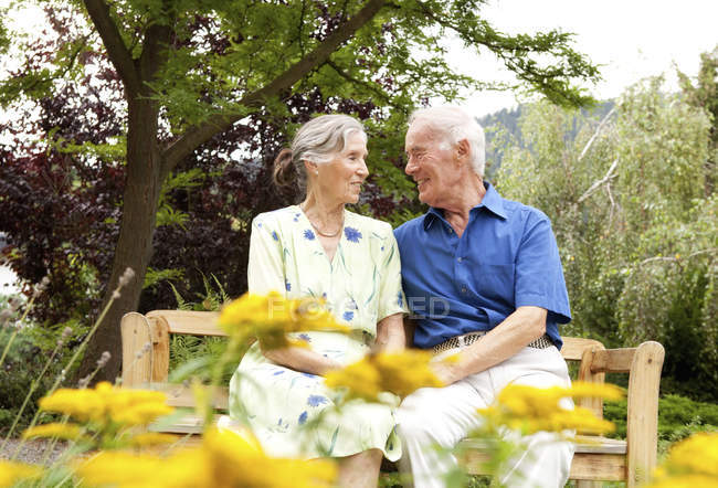 Confident senior couple sitting on bench in garden — Stock Photo