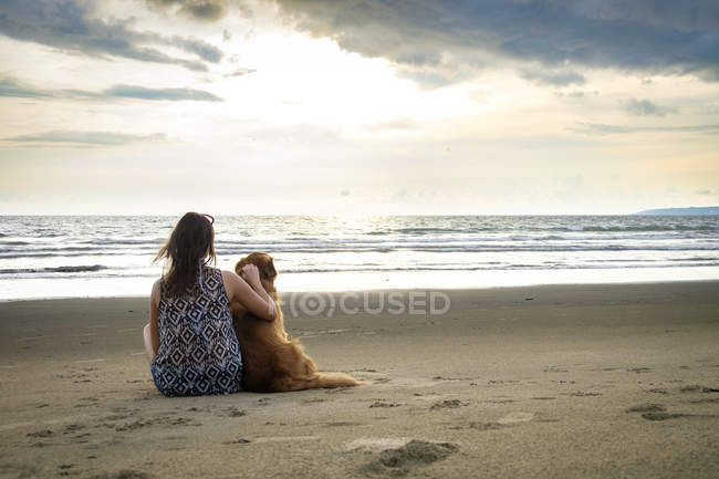 Mexiko, nayarit, Rückansicht einer jungen Frau, die neben ihrem Hund am Strand sitzt — Stockfoto