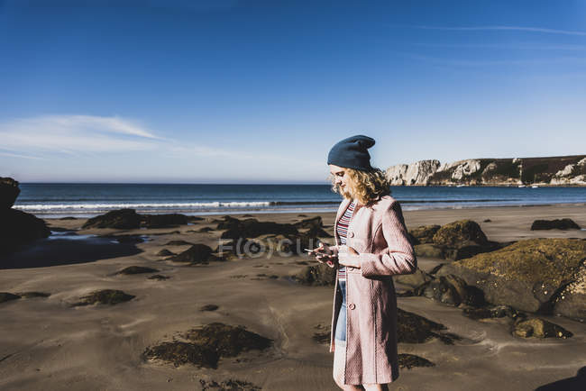 Девочка-подросток в шапочке с сотовым телефоном на пляже — стоковое фото