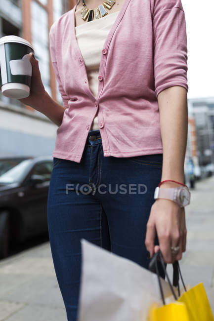 Image recadrée de fille décontractée avec tasse de café et sacs à l'extérieur — Photo de stock