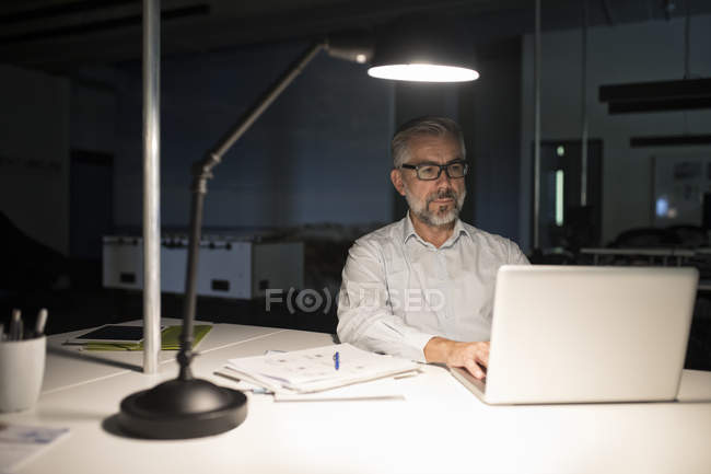 Uomo d'affari che utilizza il computer portatile al buio in ufficio — Foto stock
