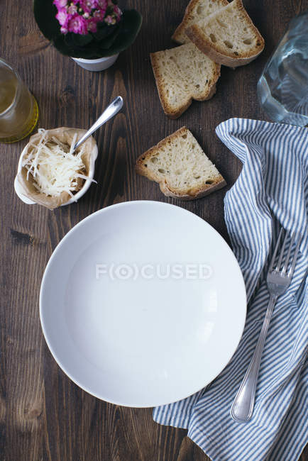Placa vacía, parmesano, rebanadas de pan blanco, tela y tenedor en madera oscura - foto de stock