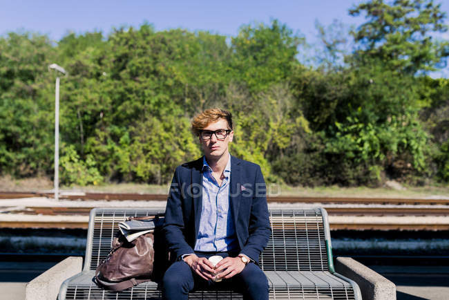 Молодий підприємець з кави, щоб піти, сидячи на лавці на платформі — стокове фото