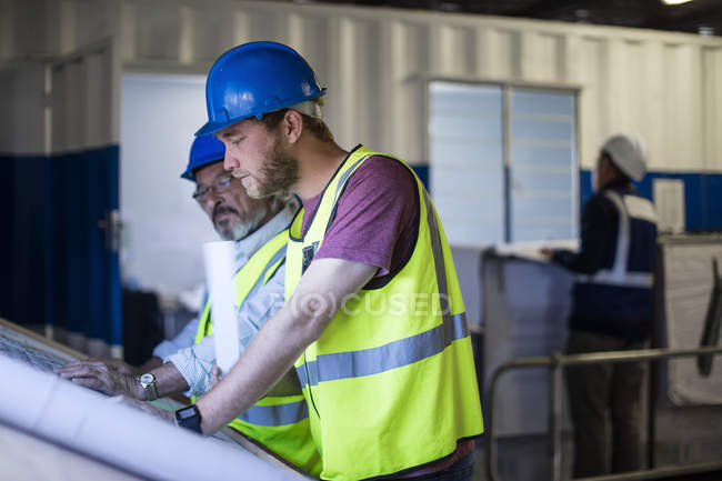 Trabalhador da construção civil e engenheiro discutindo projeto no escritório do local — Fotografia de Stock