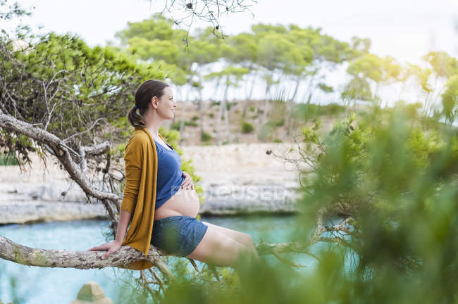 Pregnant woman sitting on branch on sea coast — Stock Photo