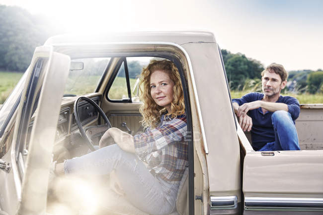 Sorridente autista di auto femminile seduto in furgone con uomo sul letto del camion — Foto stock
