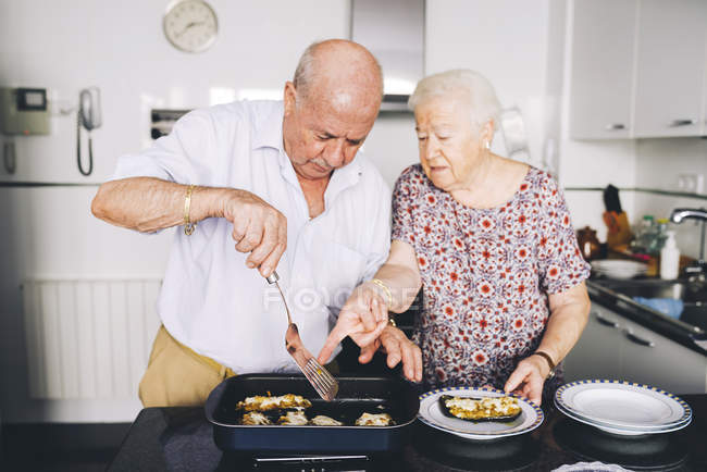 Senior couple serving stuffed eggplants in the kitchen — Stock Photo