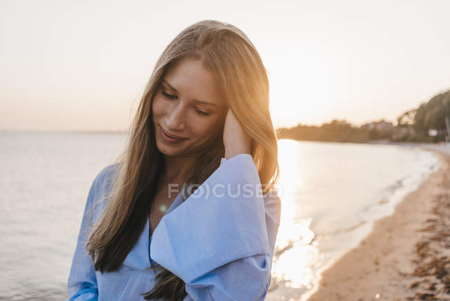 Jeune femme souriante sur la plage au coucher du soleil — Photo de stock